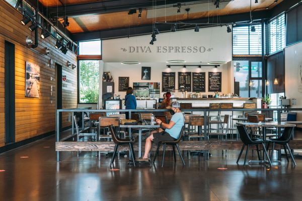 Photo inside Diva Espresso building, man sitting at table with coffee in foreground, coffee counter in background