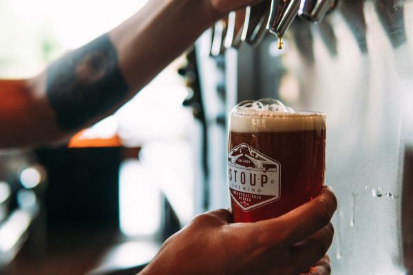 Image of man's hands holding a beer glass that says Stoup Brewing